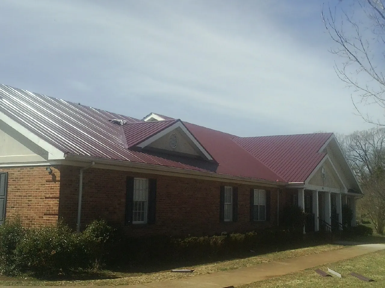 Red metal roof with gabled entries on a long brick building, from a Hail Damage Roof Repair job in Pearlington