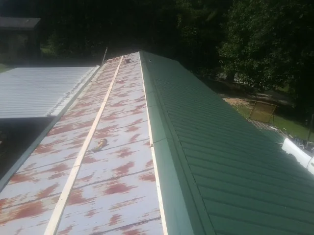 Old rusted panels beside newly installed green metal roofing — Wind Damage Roof Repair by Roofing Brothers in Pearlington