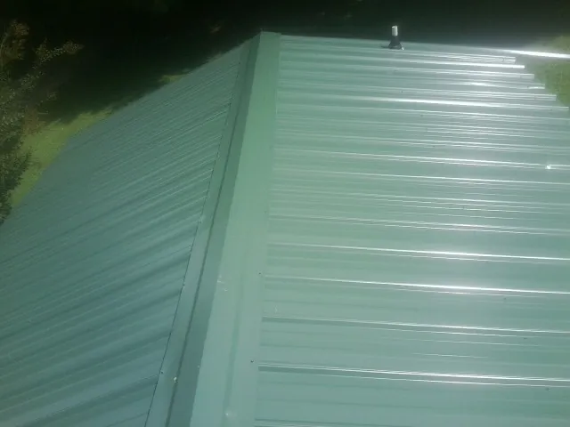 New green metal panels meeting at the ridge of a roof — Flat Roof Repair work by our crew in Pearlington