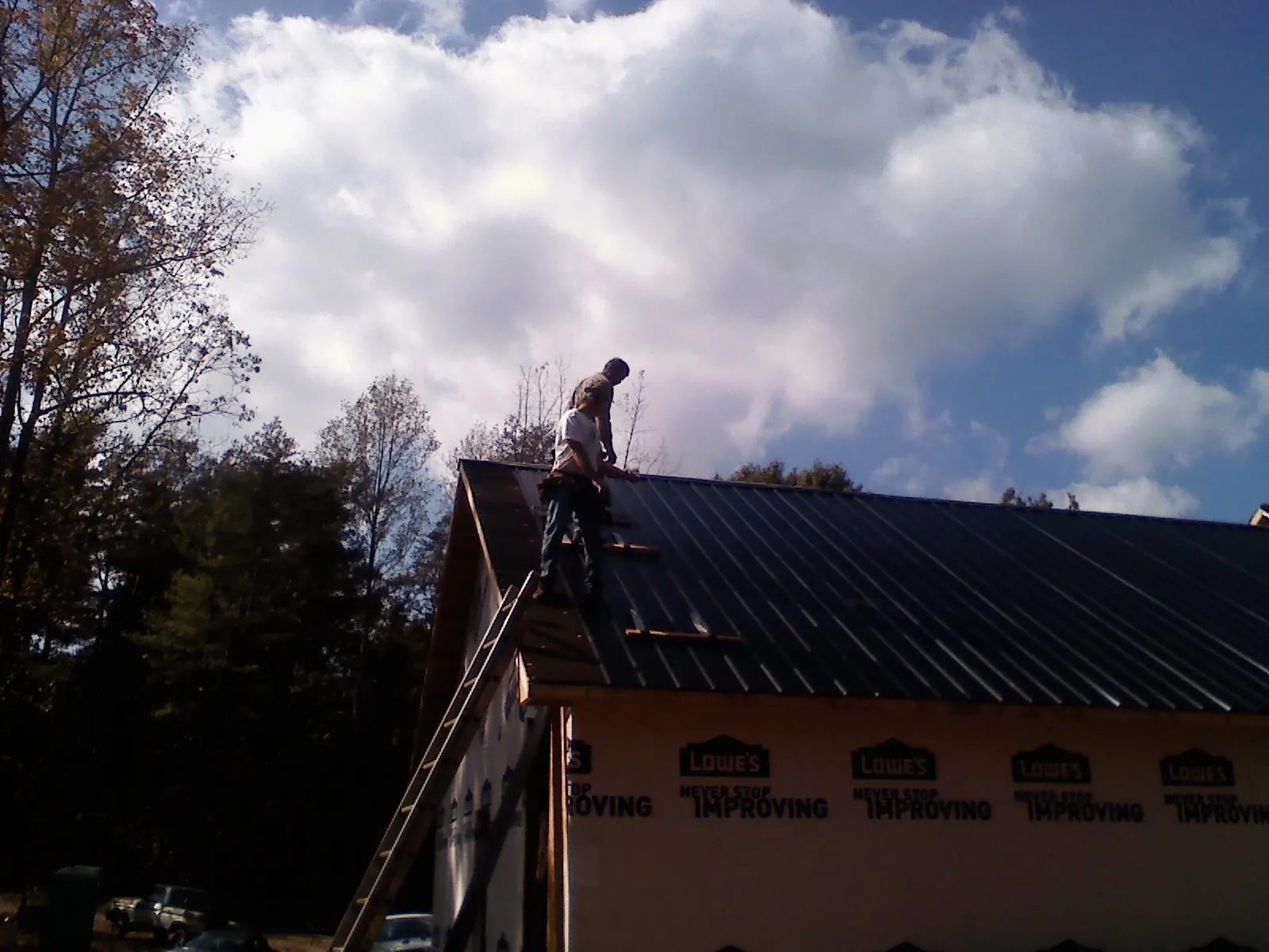 Roofer fastening dark metal panels high against a cloudy sky, from a Roof Inspection job in Pearlington