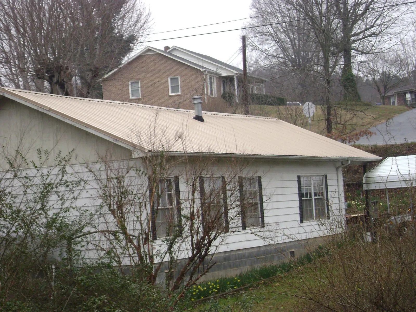 Tan metal roof on a white sided house set into a hillside — Commercial Roofing by Roofing Brothers in Pearlington