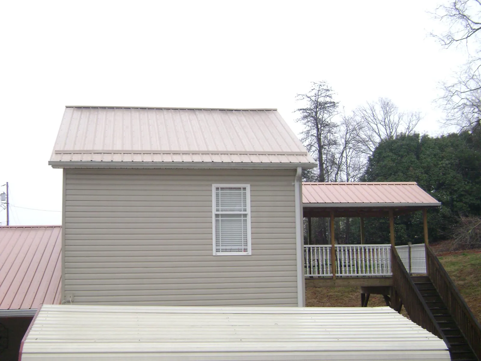 Tan metal roofs on a two story addition and attached porch, from a Roof Replacement job in Pearlington
